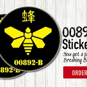 Könnte beinhalten: Zwei schwarze runde Aufkleber mit einem gelben geometrischen Bienenmuster und dem Text "00892-B". Die Aufkleber haben auch chinesische Schriftzeichen oben. Auf weißem Holzmaserung Hintergrund.