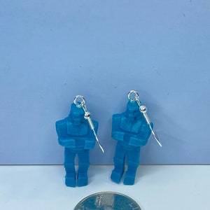 May include: A pair of blue robot earrings with silver hooks. The earrings are about the size of a quarter.