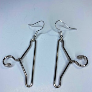 May include: A pair of silver earrings shaped like miniature hangers. The earrings have a simple, modern design and are perfect for adding a touch of whimsy to any outfit.