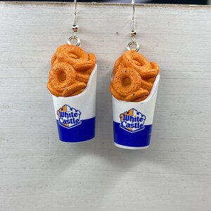 May include: A pair of earrings featuring a White Castle onion ring container with a blue and white logo. The onion rings are orange and have a realistic look.