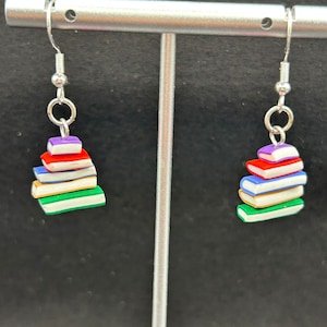 May include: A pair of silver dangle earrings with a stack of colorful books as the charm. The books are red, purple, blue, white, green, and yellow.