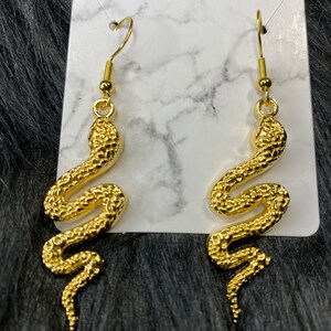 May include: A pair of gold snake dangle earrings. The snakes are detailed with a textured surface.