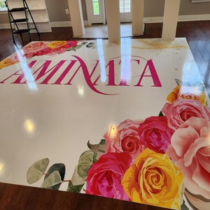 Puede incluir: Un suelo blanco con un dise&ntilde;o floral rosa y el nombre "Aminata" escrito en letras rosas. El suelo est&aacute; decorado con rosas rosas, amarillas y blancas.