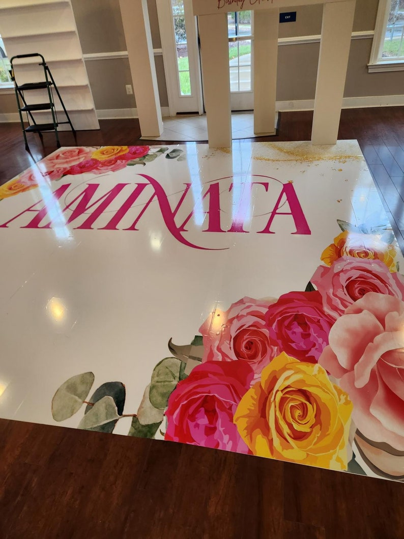 Puede incluir: Un suelo blanco con un dise&ntilde;o floral rosa y el nombre "Aminata" escrito en letras rosas. El suelo est&aacute; decorado con rosas rosas, amarillas y blancas.