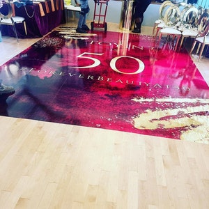 Puede incluir: Una pista de baile roja y dorada con el texto "Toy in 50 #ForeverBeautyAt50".