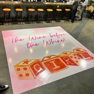Puede incluir: Una alfombra de suelo rosa y blanca con el texto "The Wine Before The Whine!" y un gr&aacute;fico de bloques de juguetes coloridos que deletrean "GIRL".