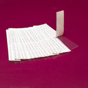 Könnte beinhalten: Ein Stapel weißer Klebebandstreifen mit dem aufgedruckten Text "STIER THIS SITE THE STATES". Das Klebeband liegt auf einer rosa Oberfläche.