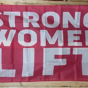 May include: A pink flag with the words "STRONG WOMEN LIFT" in white lettering.