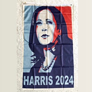May include: A blue, red, and white political campaign flag featuring a portrait of Kamala Harris with the text "HARRIS 2024".