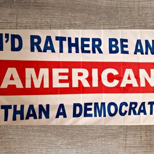 May include: A white flag with blue and red text that reads "I'd rather be an American than a Democrat".
