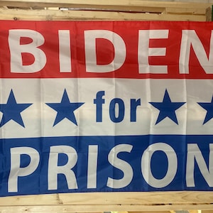 May include: A red, white, and blue flag with the text "BIDEN for PRISON" in white letters.