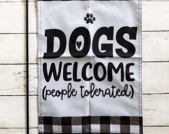 May include: A white and black checkered garden flag with the text "Dogs Welcome (people tolerated)" in black lettering. A paw print is above the word "Dogs".