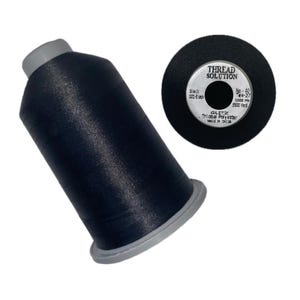 May include: A spool of black thread and a matching thread spool end. The thread is labeled "THREAD SOLUTION" and "101-Black". The spool end has the text "No-40", "EX-27", "1000 m", and "5500 yard". The thread is Trilobal Polyester.