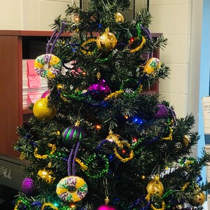 Puede incluir: Un &aacute;rbol de Navidad artificial verde decorado con adornos morados, dorados y verdes, incluyendo m&aacute;scaras de Mardi Gras, cuentas y una estrella dorada en la parte superior.