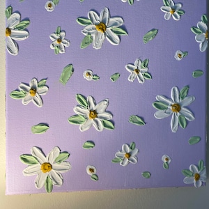 Peut inclure: Une peinture sur toile violette avec un motif de marguerites blanches. Les marguerites ont des centres jaunes et des feuilles vertes. La peinture a un aspect texturé.