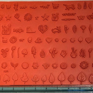 May include: A red rubber sheet with a variety of floral and leaf designs for stamping. The sheet is approximately 11 inches wide and 7 inches long.