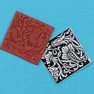 May include: Two square rubber stamps with floral designs. One stamp is a dark reddish-brown color, and the other is black with a white floral pattern. The stamps are set against a bright blue background.