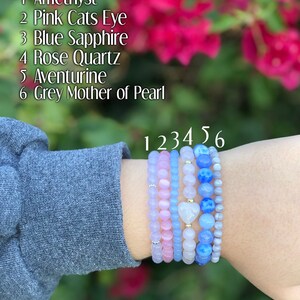 Puede incluir: Seis pulseras apiladas con cuentas de diferentes colores. Las pulseras est&aacute;n etiquetadas del 1 al 6. Las etiquetas corresponden a las siguientes piedras: Amatista, Ojo de Gato Rosa, Zafiro Azul, Cuarzo Rosa, Aventurina y Madreperla Gris.