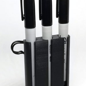 May include: A black pen holder containing three black Sharpie permanent markers. The markers are white with black caps and the words "Permanent Marker" printed on the side. The holder has a loop for attaching to a keychain or lanyard.