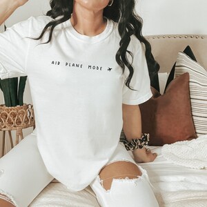 Peut inclure: T-shirt blanc avec le texte "AIR PLANE MODE" et une petite ic&ocirc;ne d'avion imprim&eacute; sur le devant.