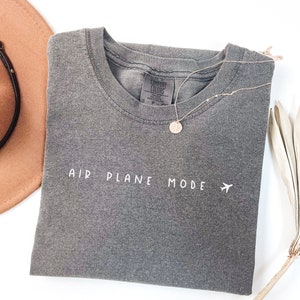 Peut inclure: T-shirt gris avec le texte "AIR PLANE MODE" et un petit avion graphique en blanc.