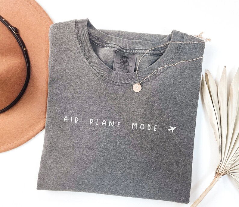 Peut inclure: T-shirt gris avec le texte "AIR PLANE MODE" et un petit avion graphique en blanc.