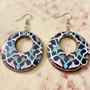 May include: A pair of wooden hoop earrings with intricate mosaic-style patterns. The earrings feature a dark blue background with white, teal, and brown geometric designs. Silver-colored ear wires complete the design.