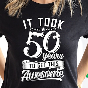 May include: Black t-shirt with white text that reads "It took 50 years to get this awesome".