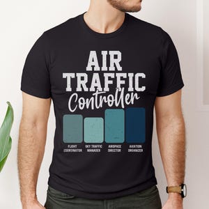 May include: Black t-shirt with the text "AIR TRAFFIC Controller" in white, above four colored rectangles. The rectangles are in shades of blue and green, with job titles below each: Flight Coordinator, Sky Traffic Manager, Airspace Director, and Aviation Organizer.