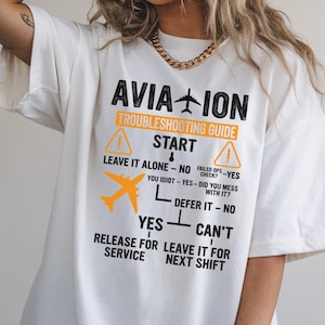 May include: White t-shirt with the text "AVIATION TROUBLESHOOTING GUIDE" in black and orange. The shirt features a diagram with an airplane graphic and phrases like "Leave it alone" and "Defer it".