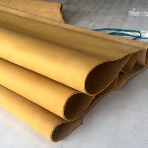 May include: Close-up of a stack of four pieces of light brown leather. The leather is rolled up and has a smooth, even texture.