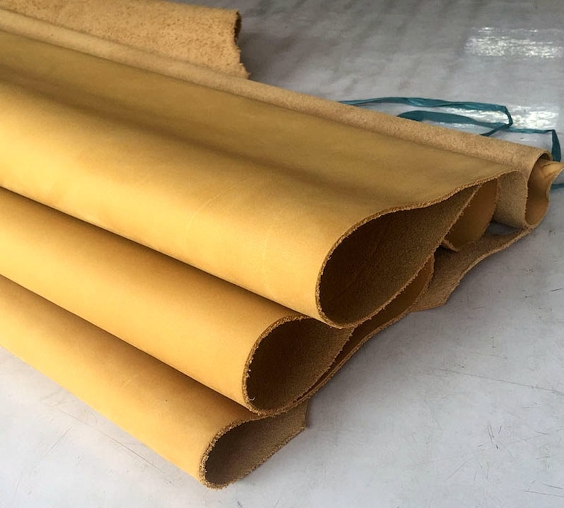 May include: Close-up of a stack of four pieces of light brown leather. The leather is rolled up and has a smooth, even texture.