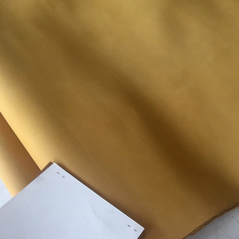 May include: A close-up of a smooth, mustard yellow fabric. The fabric is folded and has a slight sheen.