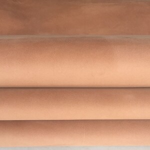 May include: Close-up of a folded piece of light brown leather. The leather has a smooth, velvety texture.