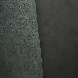 May include: Close-up of two pieces of dark gray leather. One piece has a smooth surface, while the other has a textured surface.