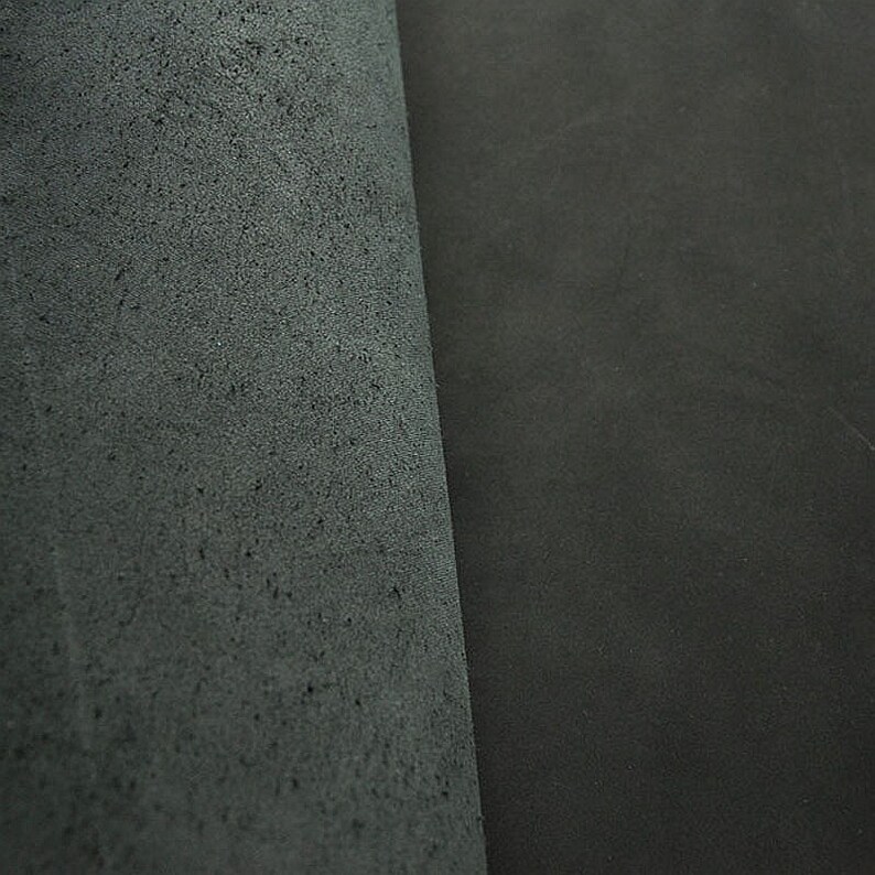 May include: Close-up of two pieces of dark gray leather. One piece has a smooth surface, while the other has a textured surface.