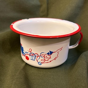 May include: White enamelware cup with a red rim and a blue and white cat design. The cat is playing with a ball of yarn.