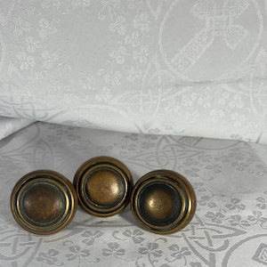 May include: Three antique brass cabinet knobs with a raised circular design. The knobs have a slightly aged, tarnished look.