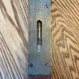 May include: A vintage brass level with a wooden handle. The level is marked "No. 000 STANLEY RULE & LEVEL CO. NEW BRITAIN, CONN. U.S.A."