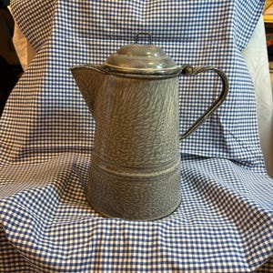 May include: A gray enamelware coffee pot with a speckled finish and a blue and white checkered tablecloth.