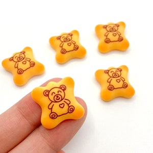 May include: Five yellow star-shaped cookies with a brown teddy bear design. The cookies are about 1 inch in diameter.