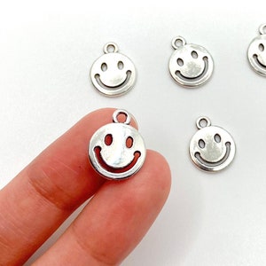 Puede incluir: Seis colgantes de plata con forma de cara sonriente. Los colgantes miden aproximadamente 1 cm de diámetro.