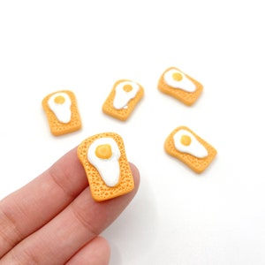 May include: Five miniature orange and white ceramic egg and toast charms. The charms are about 1 inch in size.