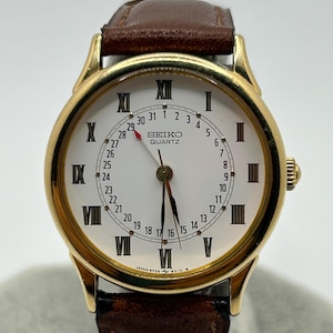 May include: A gold-toned Seiko Quartz watch with a white face, black Roman numerals, and a brown leather band. The watch displays the date and time, with the brand name visible on the face.