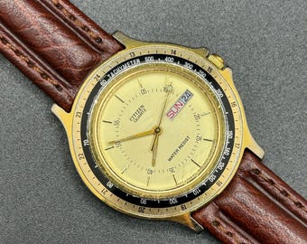 Reloj Citizen 6100-S15877 vintage con fecha y día, bisel taquimétrico dorado, correa de piel marrón, reloj de cuarzo para hombre.