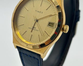 Reloj de vestir Timex vintage para hombre, tono dorado, con bisel festoneado y mecanismo mecánico de cuerda manual.