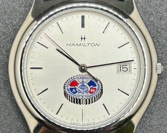 Reloj Hamilton vintage para hombre, fabricado en Suiza, con esfera plateada, ventana de fecha y logotipo "International Association Of Machinists And Aerospace Workers".
