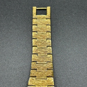 May include: A gold-toned metal watch band featuring a textured, bark-like finish on each rectangular link. The band is composed of multiple interlocking segments that taper slightly toward the top, ending in a simple rectangular clasp connector.