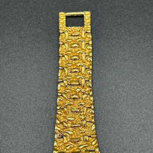 May include: A gold-toned watch band featuring a textured, nugget-style link design. The metal strap consists of multiple interconnected segments with a rough, uneven surface finish, tapering slightly toward the top where a rectangular clasp is visible.