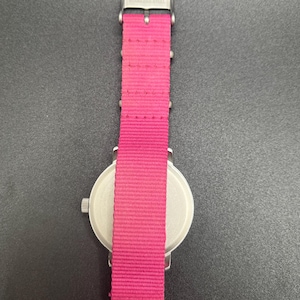 May include: A wristwatch with a bright pink nylon band and a stainless steel case. The watch has a silver-colored dial and a buckle closure. The band is approximately 0.75 inches wide.
